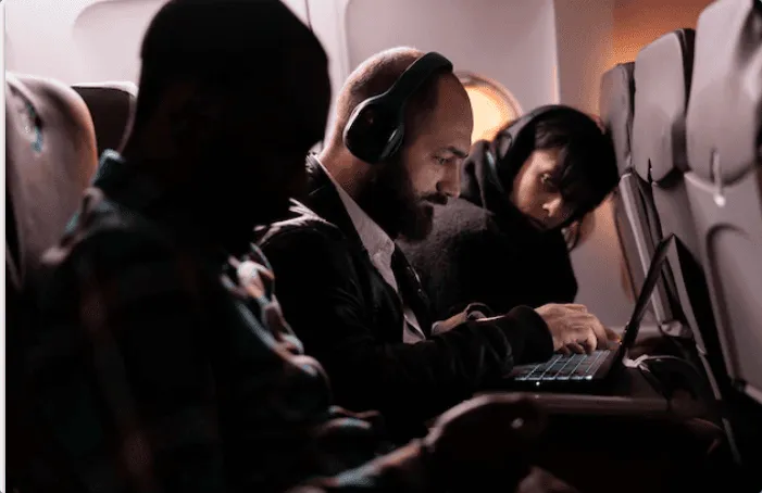 A traveller responding to an RFP on a laptop from the middle seat of a red-eye flight